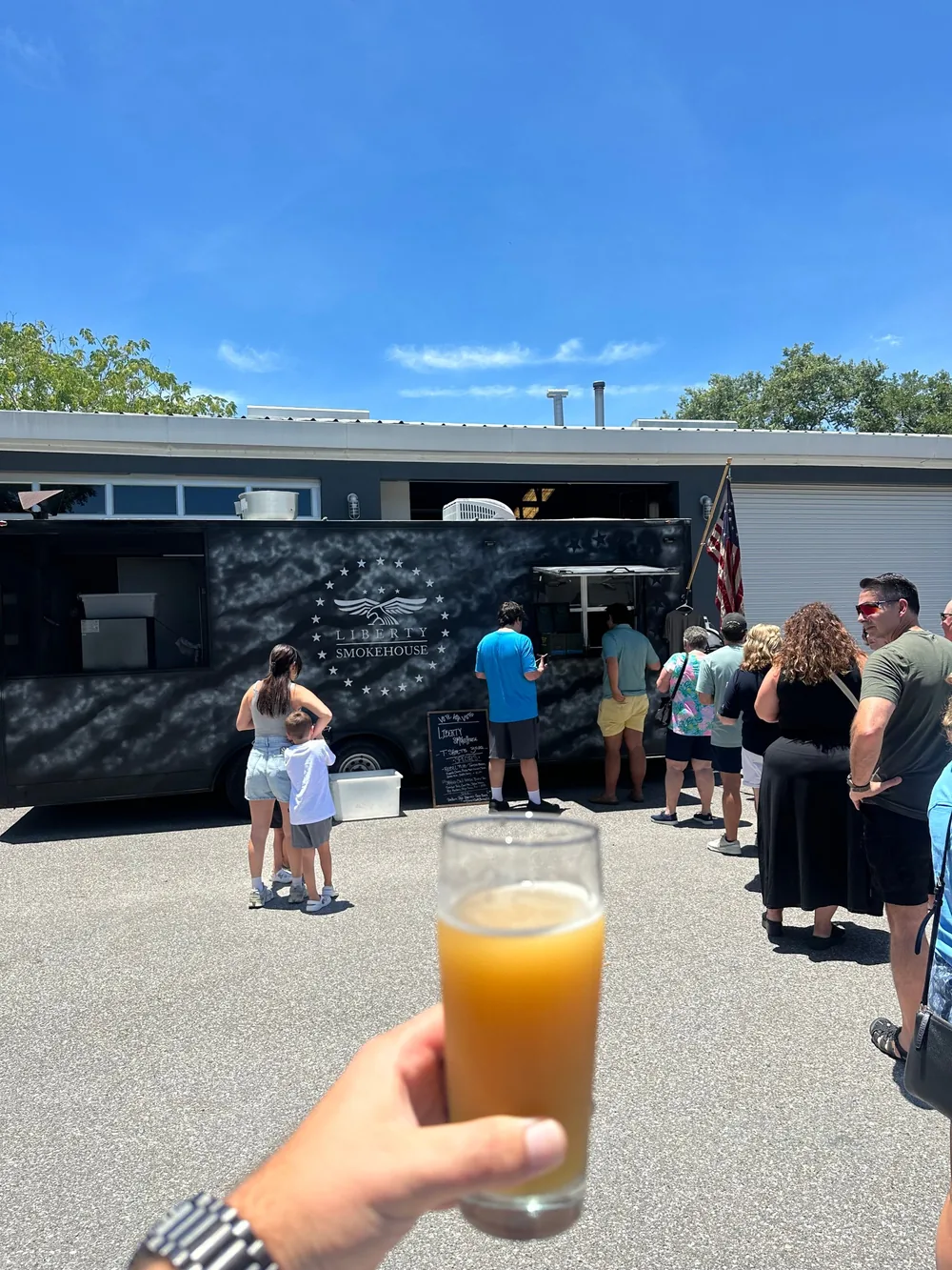 A pint raised in front of the Liberty Smokehouse trailer with a line at the window