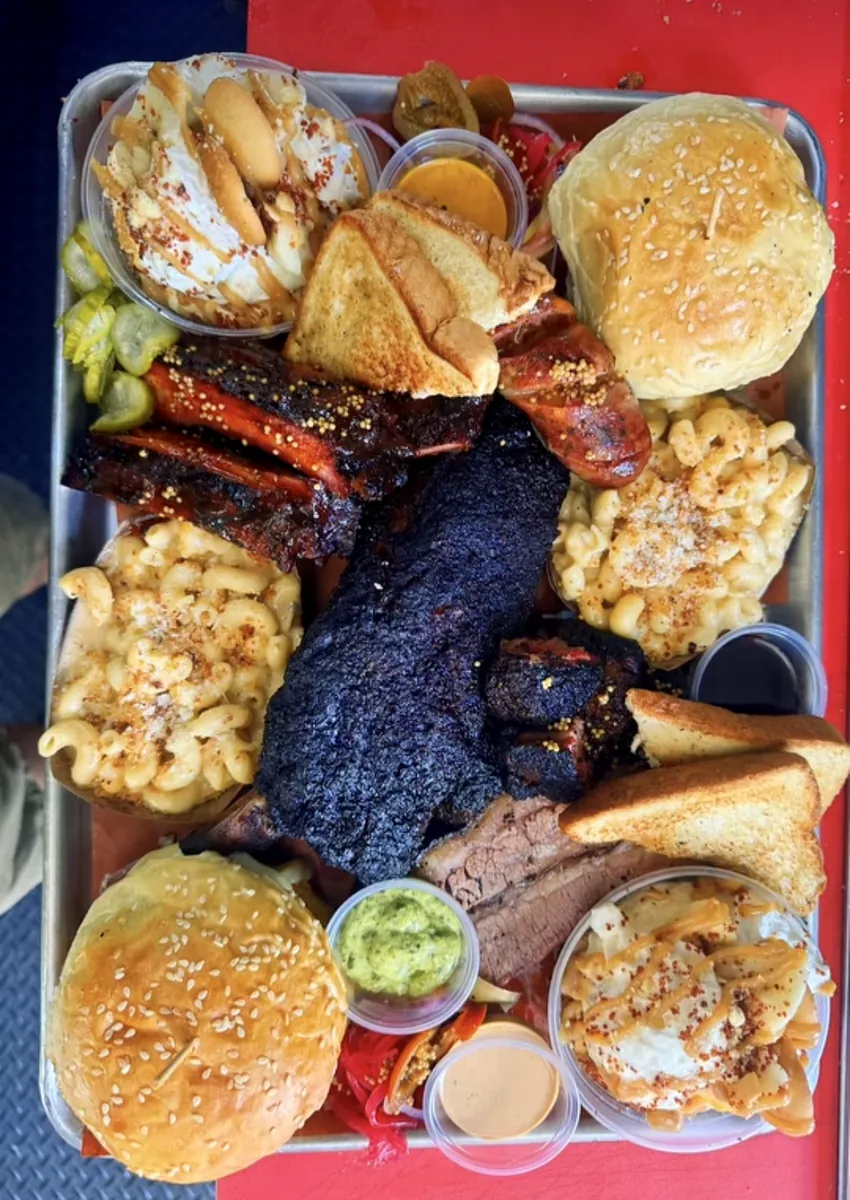 An overhead tray of brisket, ribs, sausage, burgers, mac and cheese and banana pudding